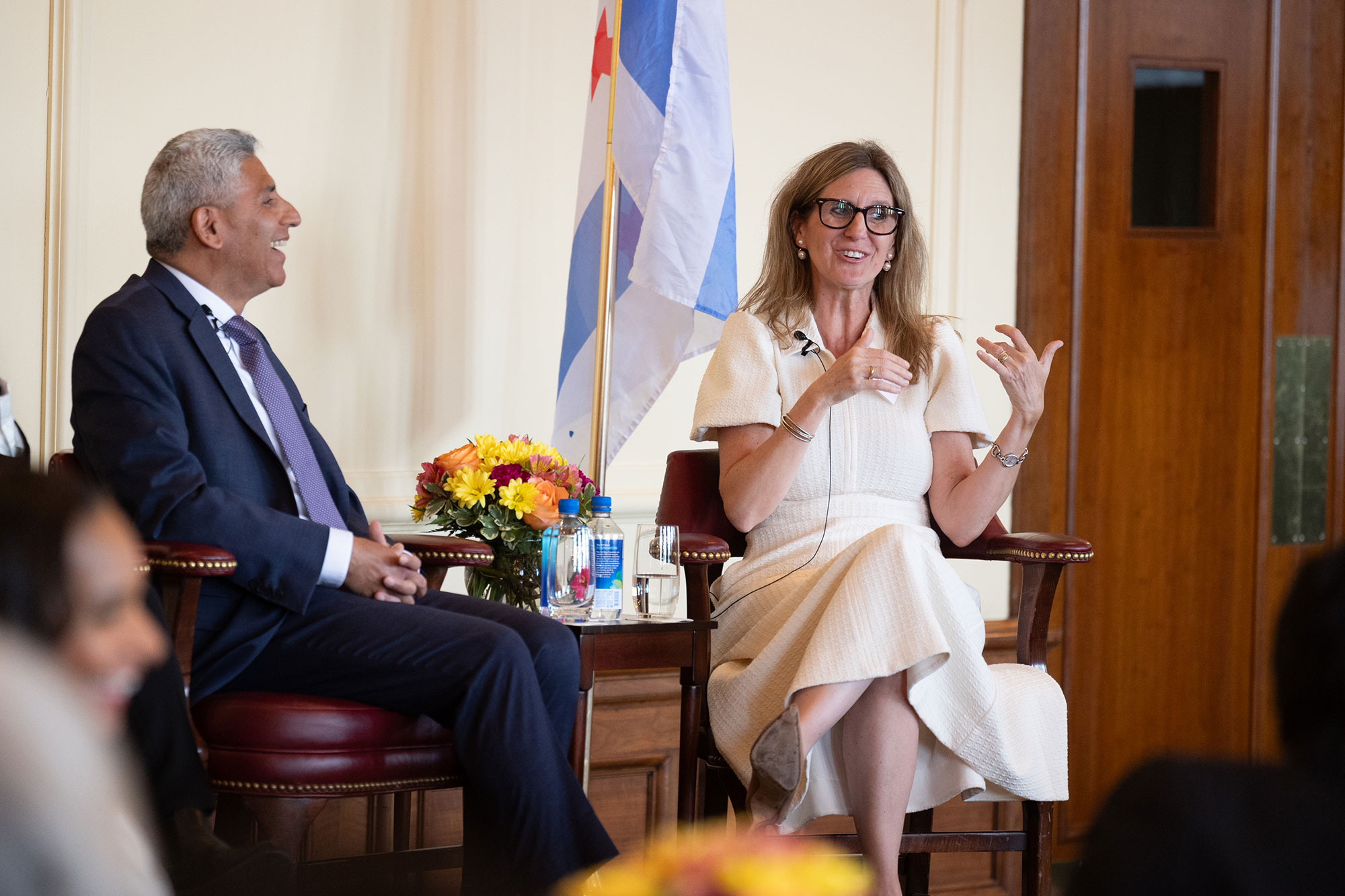 Two people talk while sitting in chairs on stage