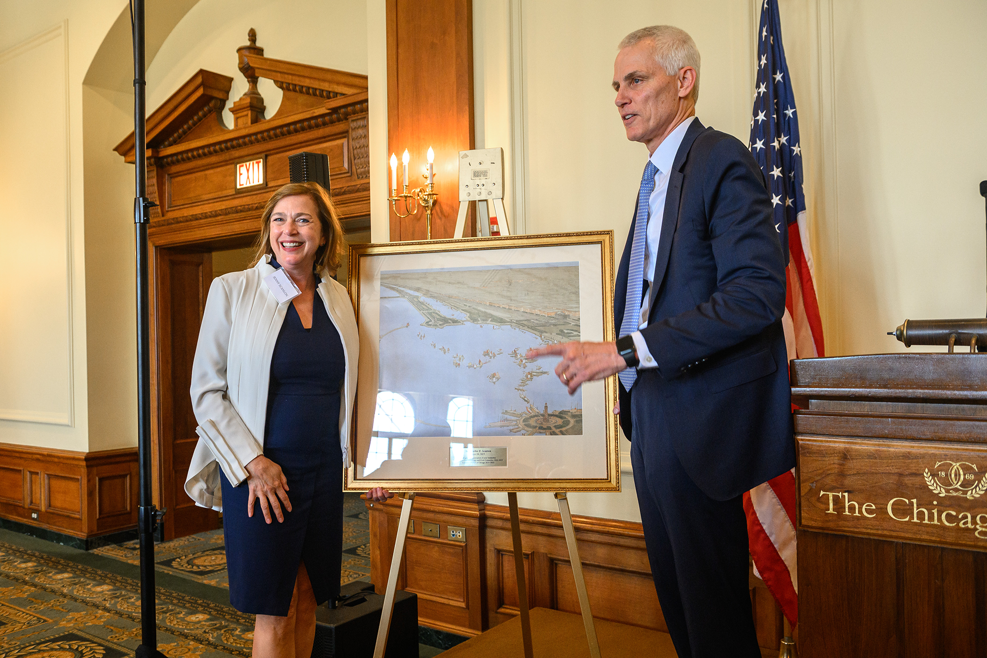 Two people stand together on stage, presenting a framed image