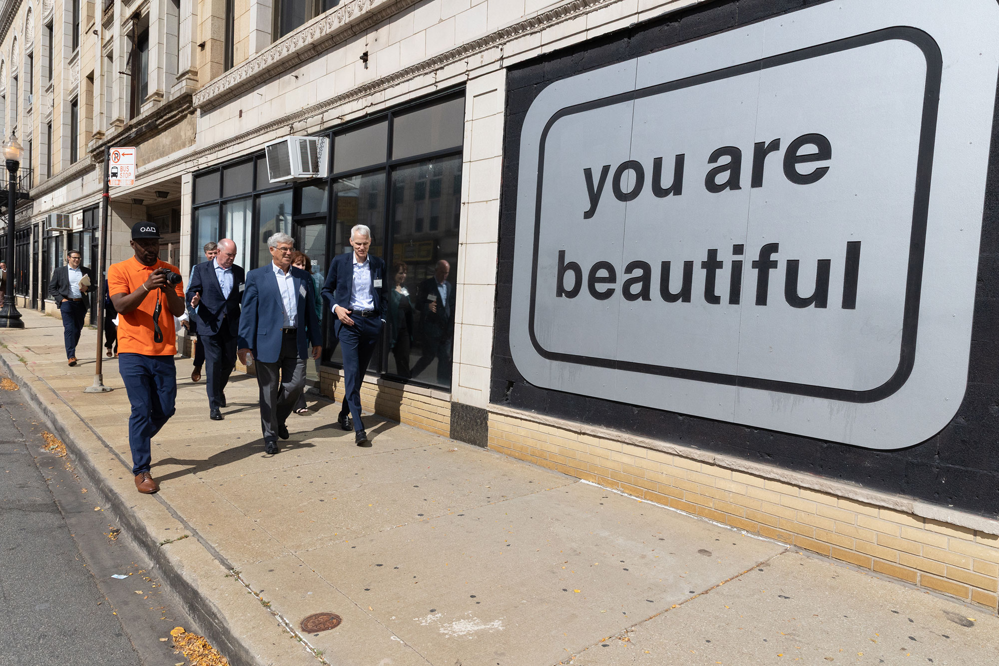 People walk in front of a large sign reading "you are beautiful"