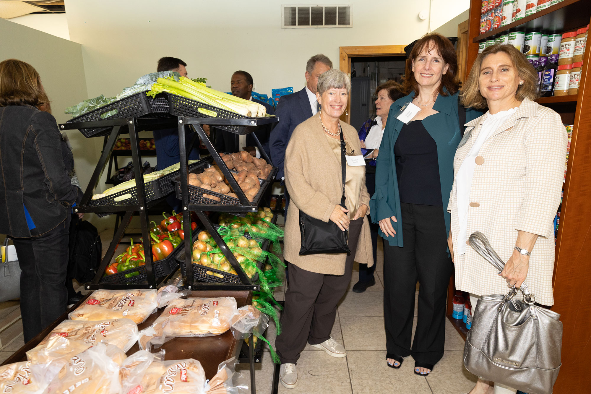 Three people smile and pose next to a shelf of fresh produce