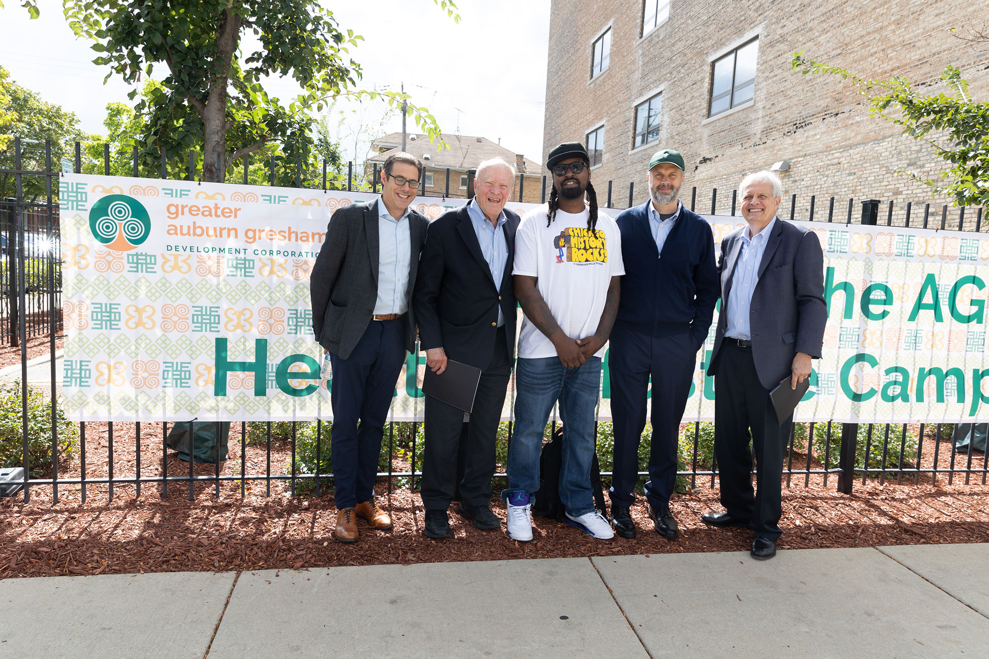 Five people stand together, in front of outdoor signs