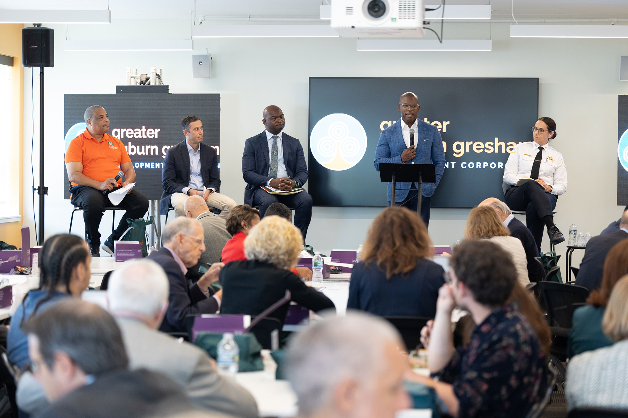 5 people speak on-stage while a crowd listens