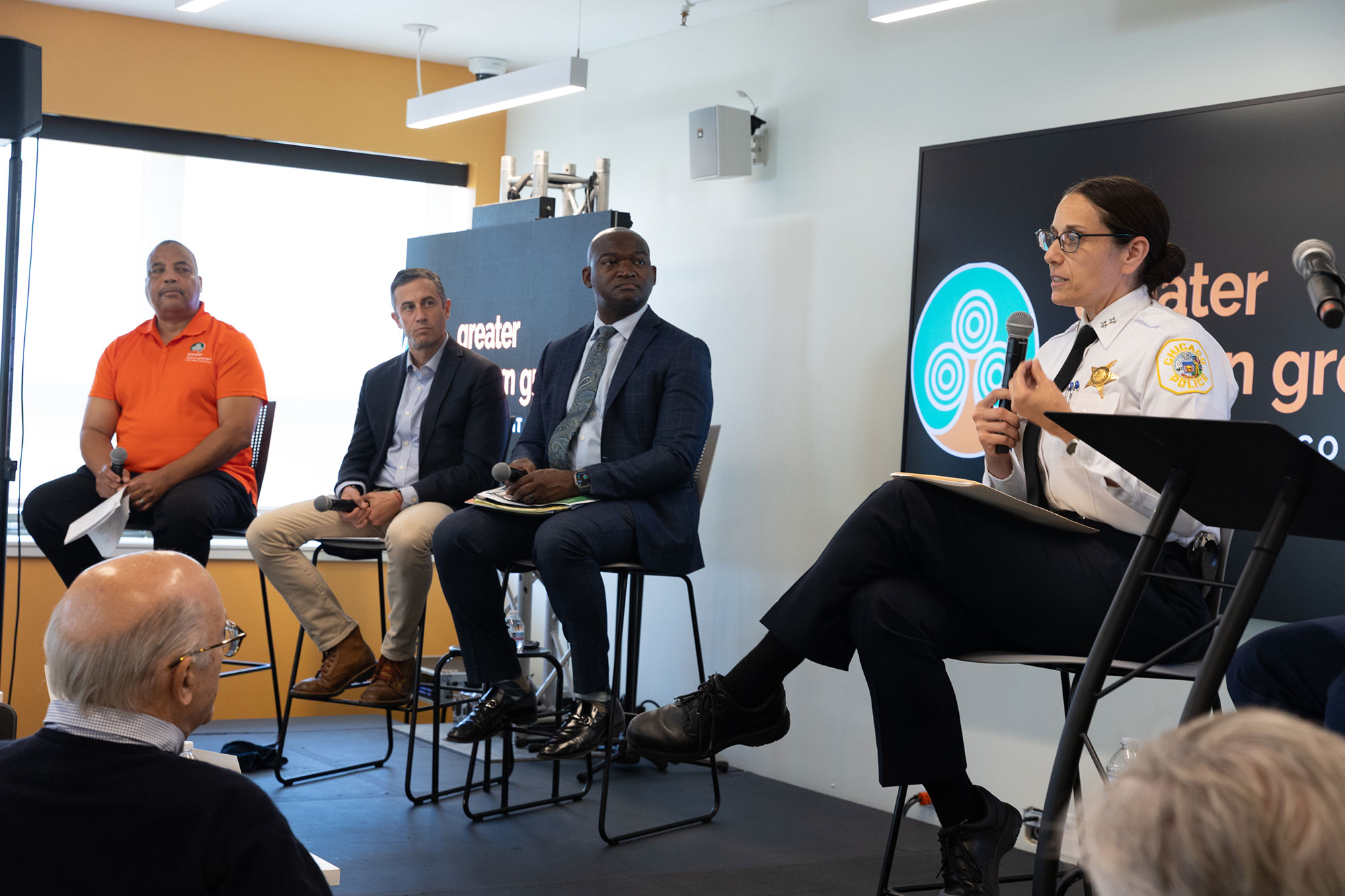 Four people sit in chairs while talking on a stage
