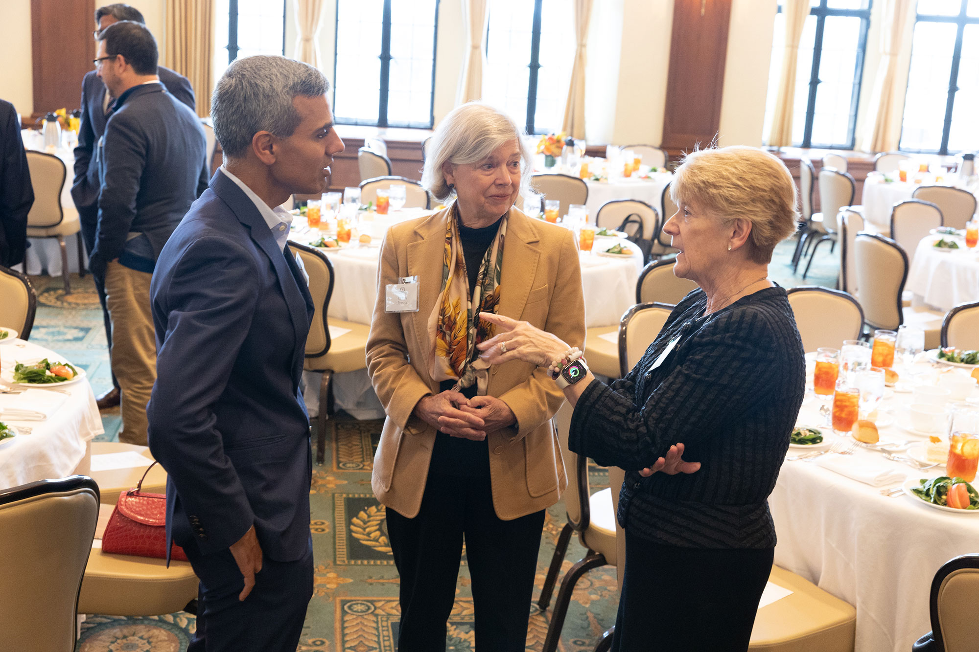 Three people stand together talking in front of dining tables