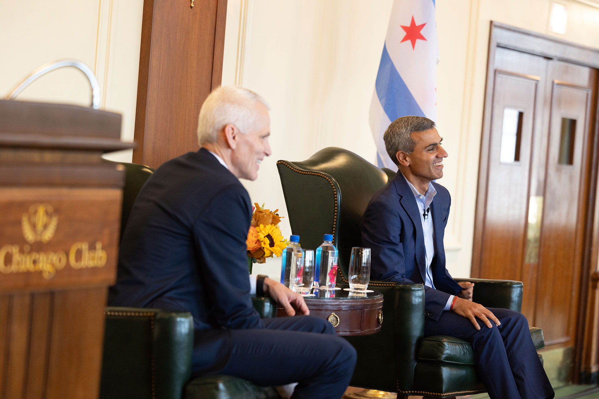 Two people talk on stage while sitting in chairs