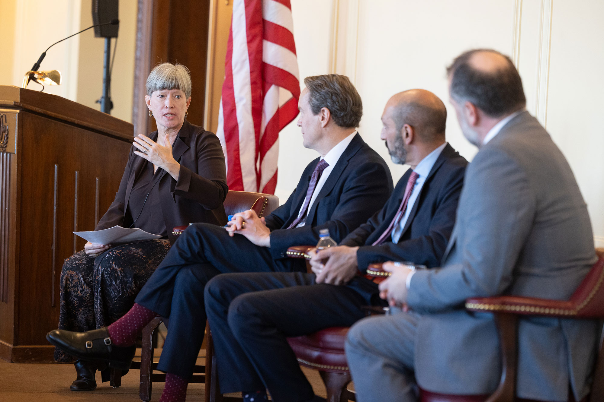 3 people sit in chairs on stage while listening to someone speak