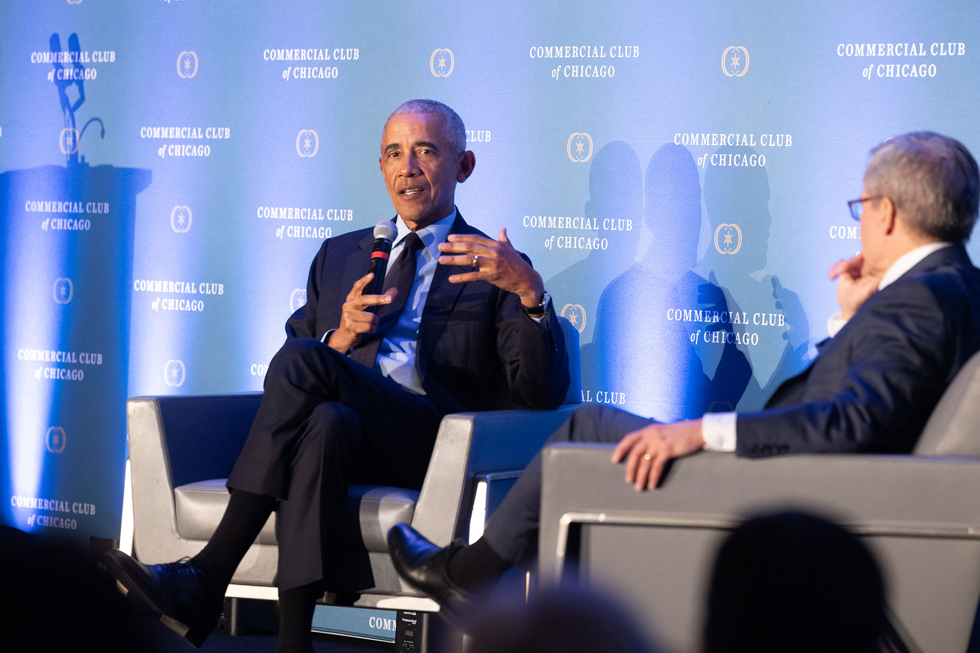 President Obama sits in a chair on-stage while speaking into a microphone