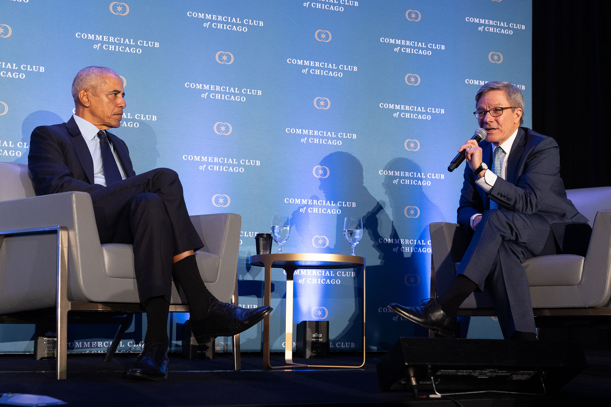 Two people sit in chairs on stage