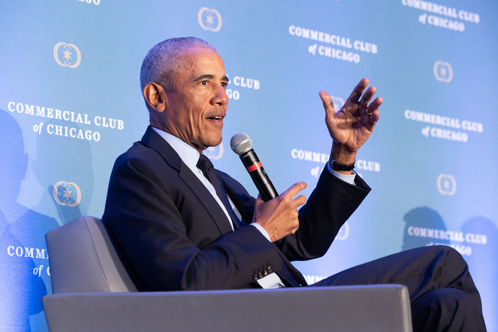 President Obama speaks into a microphone while sitting in a chair on stage