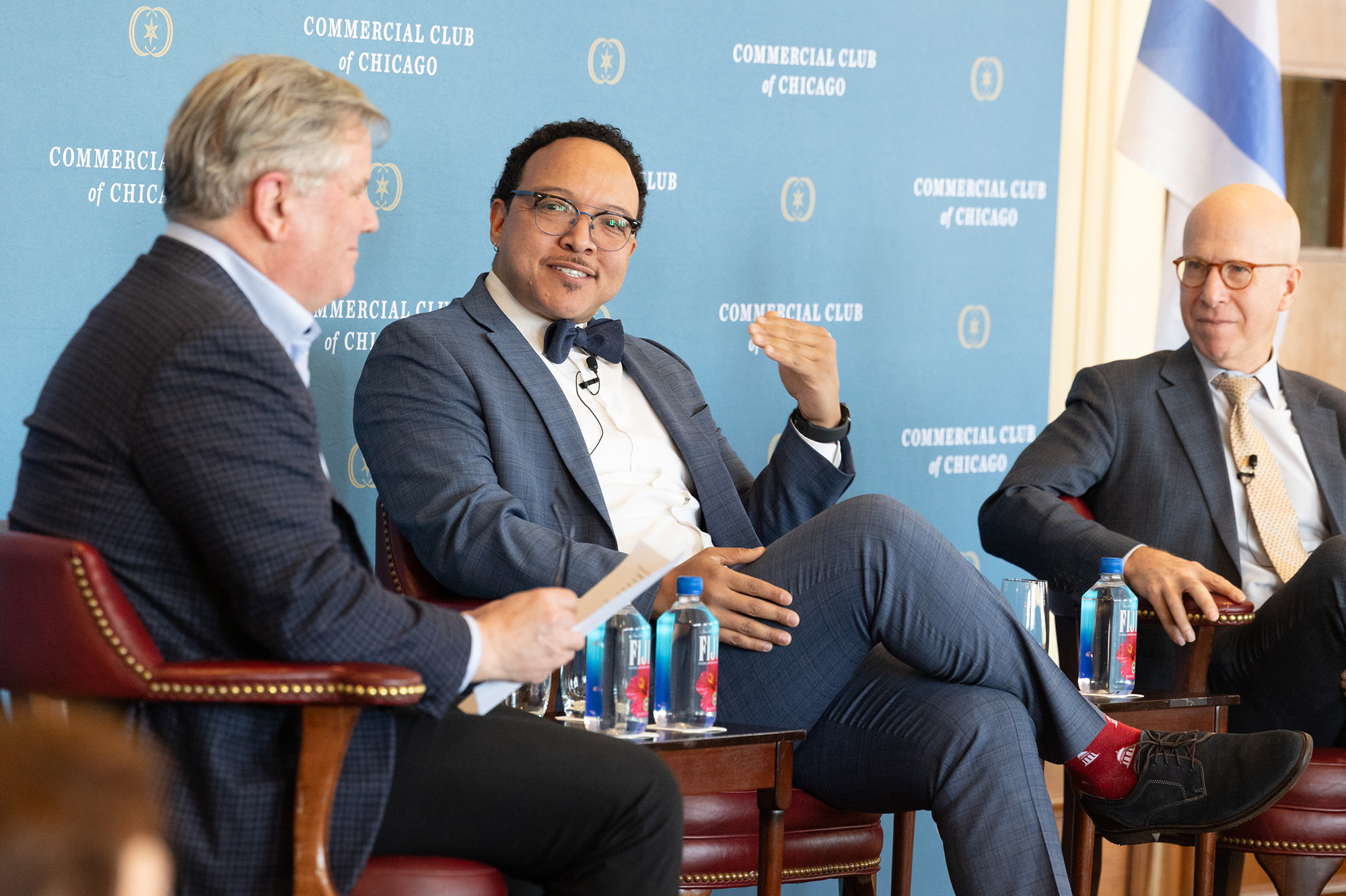 Three people sit in chairs while talking on stage