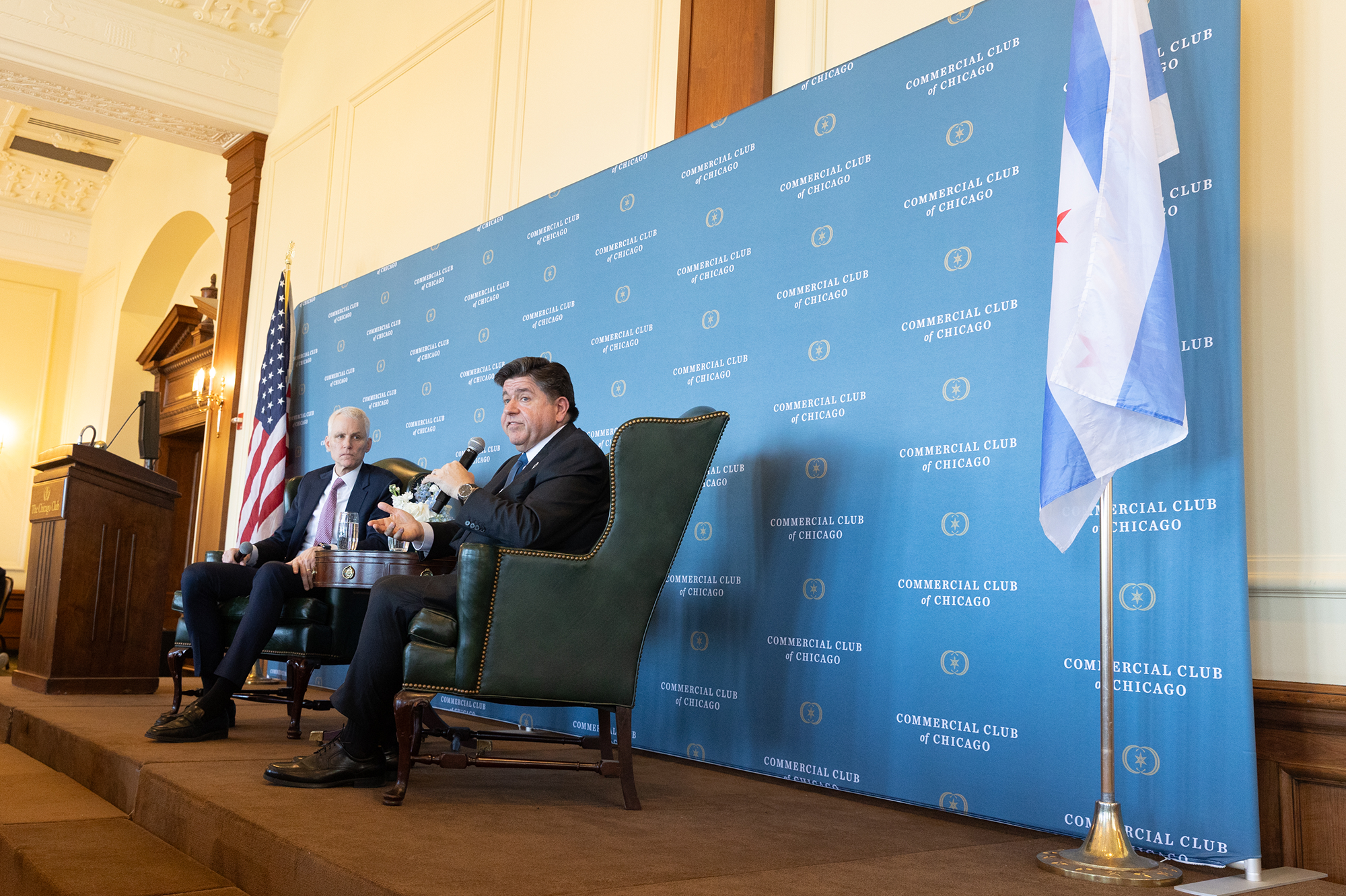 Two people sit in chairs on stage