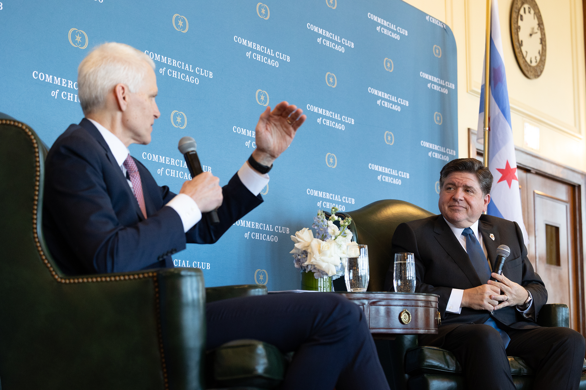 Two people sit in chairs on stage