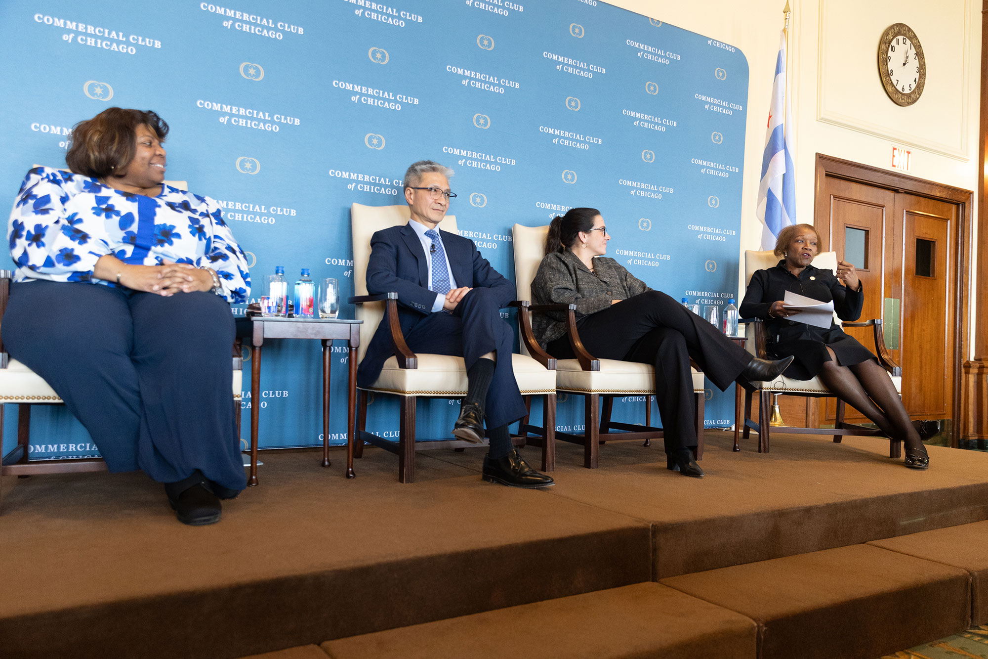 Four people sit in chairs on stage